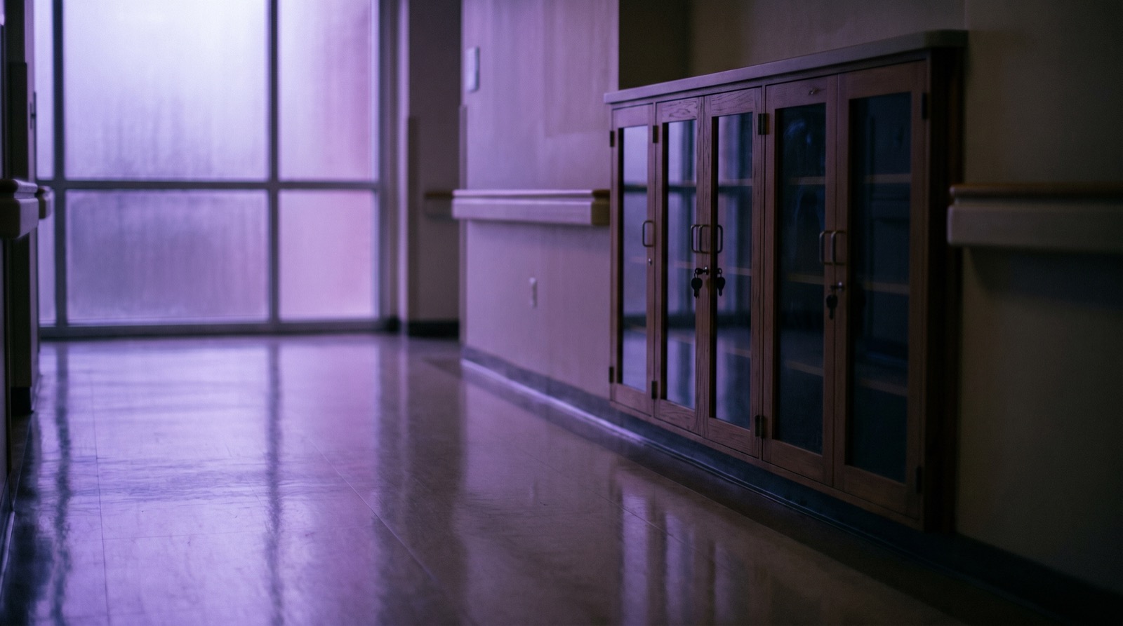 Empty hospital corridor with a medication cabinet along the wall, soft violet ambient light from frosted windows, polished floor, no people, no text visible